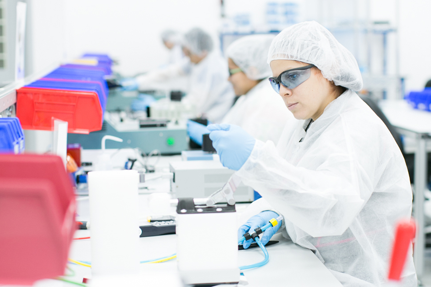 A team of lab technicians in cleanroom garments working meticulously with laboratory equipment in a high-tech contract manufacturing facility.